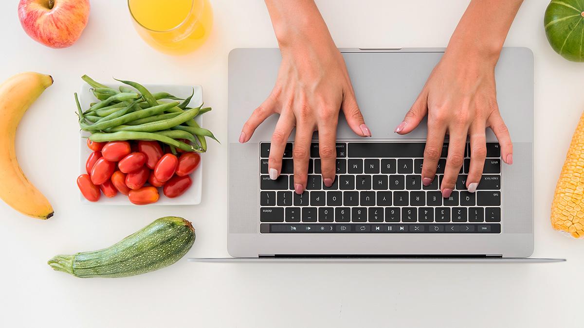 Hände auf einer Laptoptastatur, Gemüse und Früchte