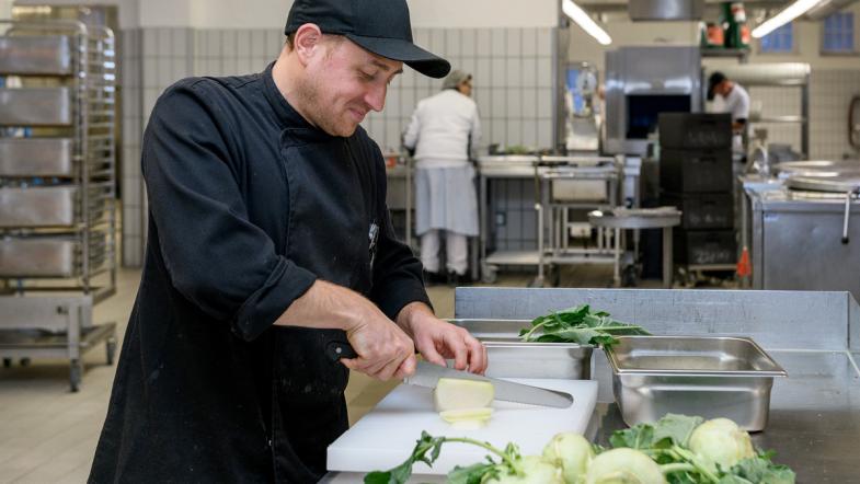 Ein Mitarbeiter der Kantine schneidet Kohlrabi.