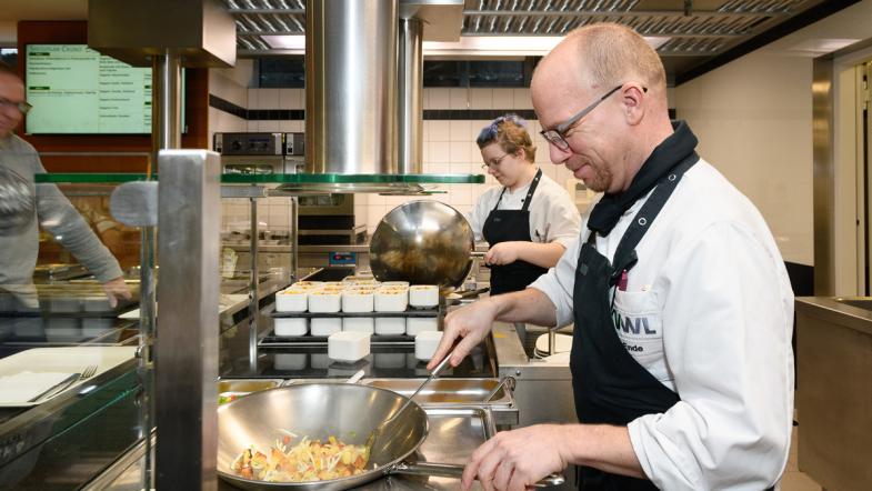 An der Essensausgabe wird in einem Wok gekocht